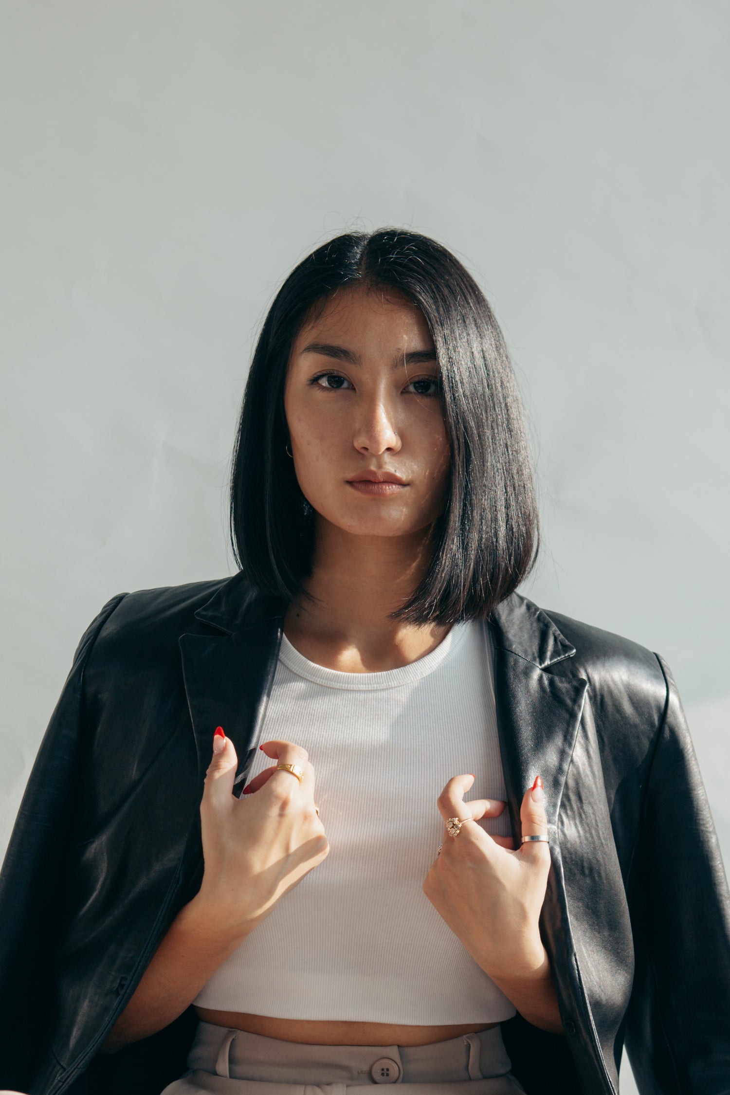 A woman with short black hair is wearing a crop white rounded neck tee with a black leather jacket.